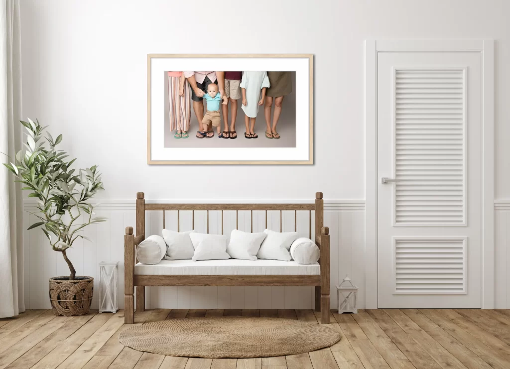 Framed family portrait of legs and feet with a toddler in the center, displayed above a wooden bench in a casual white and wood entryway