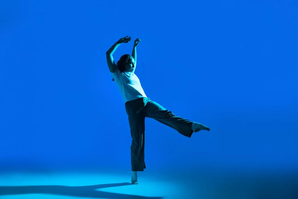 Dancer under saturated blue lighting on a studio stage with dramatic shadow and motion