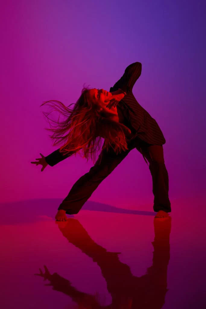 Dancer striking a pose in purple and red light with flowing hair and pinstripe suit