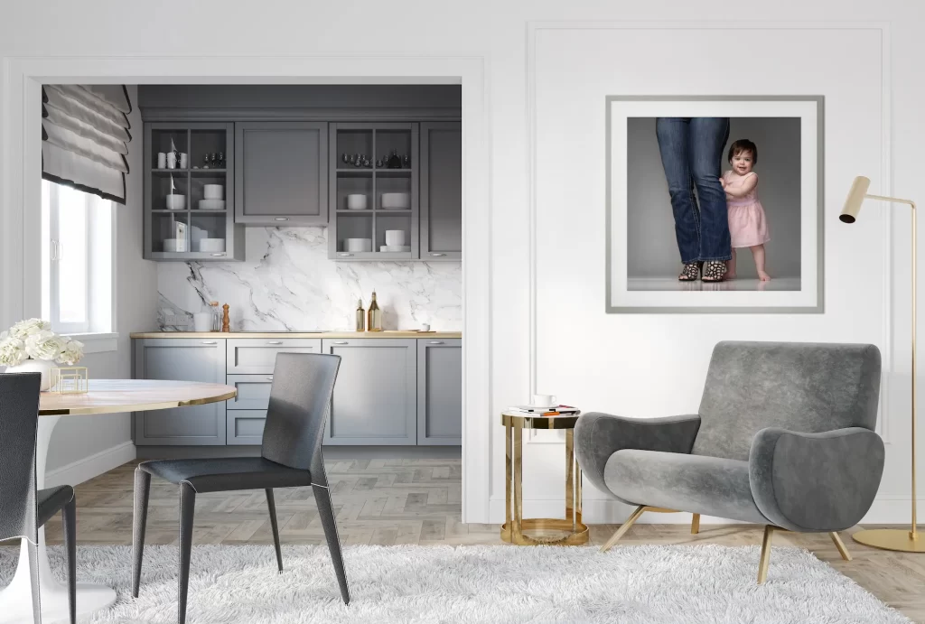 Framed portrait of a toddler hugging a parent's leg displayed in a modern gray and gold living room near a marble kitchen
