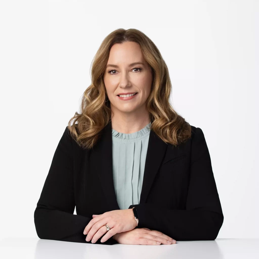 Studio headshot of a professional woman with long wavy hair in a black blazer, seated at a white table with a soft smile, photographed by Jenny E Photography in Ocala, Florida